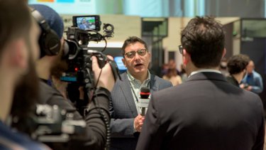 A person talks into a microphone with a film crew in the foreground while at WTCE